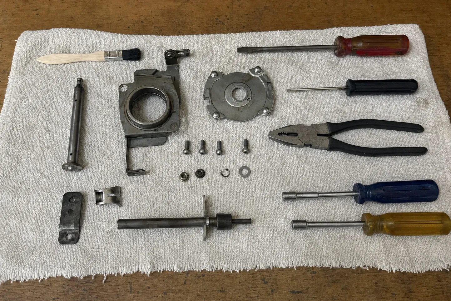 Blower motor laid out in pieces on a cloth: shaft, bearing housing with the ball bearing seated, end plate, screws and hand tools